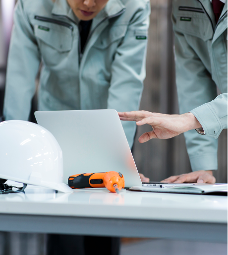 作業着を着た男性2人がPCを見ながら打ちあわせをしている様子 イメージ写真